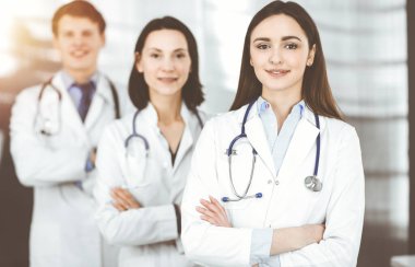 Group of young professional doctors standing as a team with arms crossed in sunny hospital. Medical help, insurance in health care, best disease treatment and medicine concept clipart