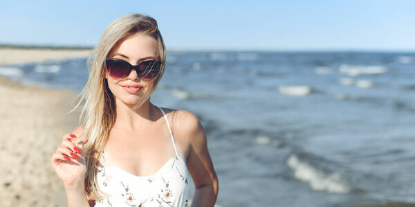 Happy blonde woman in free happiness bliss on ocean beach standing with sun glasses.