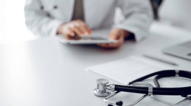 Steteskop doktorların masasında yatıyor, kapat. Doktor arka planda tablet bilgisayar kullanıyor. Tıp konsepti.