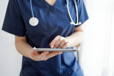 Doktor kadın panorama penceresinin yanında dururken tablet bilgisayar kullanıyor, kapatın. Doktor ya da cerrah iş başında. Tıp konsepti.