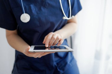 Doktor kadın panorama penceresinin yanında dururken tablet bilgisayar kullanıyor, kapatın. Doktor ya da cerrah iş başında. Tıp konsepti.