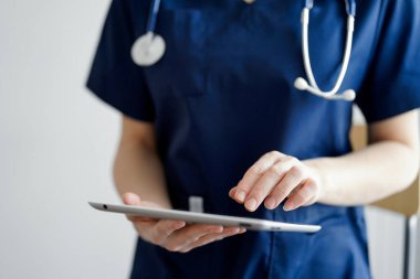 Doktor kadın panorama penceresinin yanında dururken tablet bilgisayar kullanıyor, kapatın. Doktor ya da cerrah iş başında. Tıp konsepti.