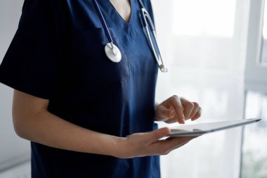 Doktor kadın panorama penceresinin yanında dururken tablet bilgisayar kullanıyor, kapatın. Doktor ya da cerrah iş başında. Tıp konsepti.