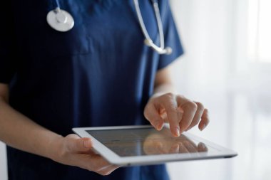 Doktor kadın panorama penceresinin yanında dururken tablet bilgisayar kullanıyor, kapatın. Doktor ya da cerrah iş başında. Tıp konsepti.