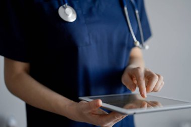 Doktor kadın panorama penceresinin yanında dururken tablet bilgisayar kullanıyor, kapatın. Doktor ya da cerrah iş başında. Tıp konsepti.