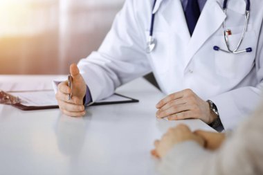 Bilinmeyen bir erkek doktor ve hasta kadın karanlık bir klinikte otururken bir şey tartışıyorlar, arka planda ışık parlıyor. Ellerin yakın çekimi.
