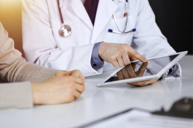 Bilinmeyen bir erkek doktor ve hasta kadın karanlık bir klinikte tablet bilgisayar kullanırken bir şeyi tartışıyor, arka planda ışık parlıyor. Hastanedeki en iyi sağlık hizmeti, ilaç, salgın durdurma.