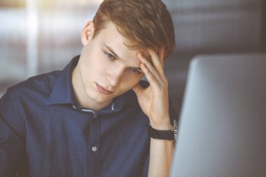 Genç sarışın iş adamı, karanlık bir ofiste iş yerinde stres hissediyor ve arka planda ışık parlıyor. Girişim işi çok çalışmak ve zamanın dışına çıkmak demektir..