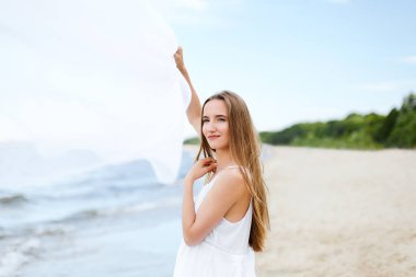 Okyanus sahilinde bulut yakalayan mutlu, mutlu, mutlu bir kadın. Beyaz yaz elbisesi içinde çok kültürlü bir kadın modelin portresi açık havada tatil sırasında doğanın tadını çıkarıyor..