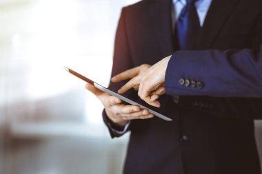 İş adamları yeni projelerini tartışmak için bir tablet bilgisayar kullanıyorlar, güneşli modern ofiste duruyorlar. İş yerinde iş arkadaşı olan tanınmamış bir işadamı ya da erkek girişimci.