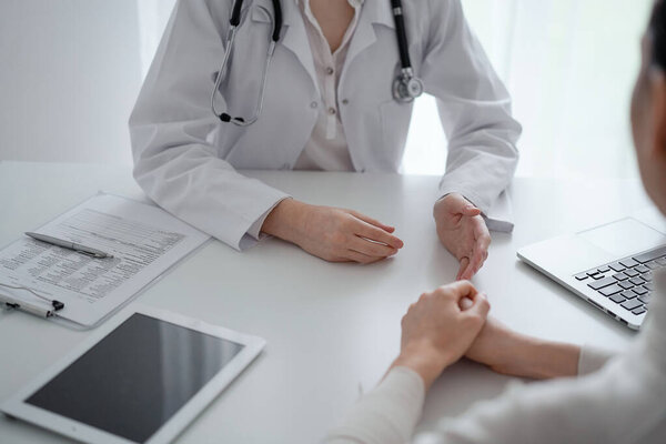 Doctor and patient discussing current health questions while sitting at the desk in clinic office, closeup. Medicine and healthcare concept.