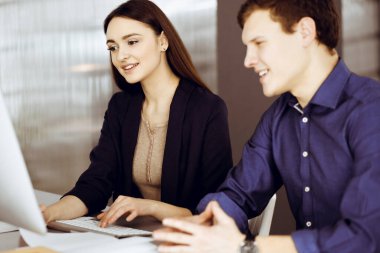 Çalışma masasında birlikte otururken iş yerindeki genç ve dost canlısı iş adamları. Kadınlara odaklan. Modern bir ofiste vesikalık ya da iş portresi.