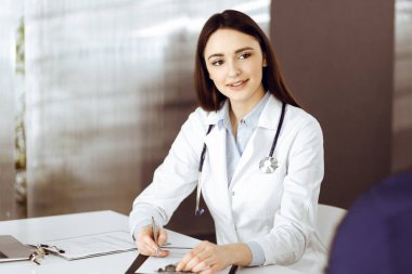 Gülümseyen genç bayan doktor, tıbbi önerileri bir not panosuyla dolduruyor. Klinikte çalışan bir terapist. Tıp konsepti.
