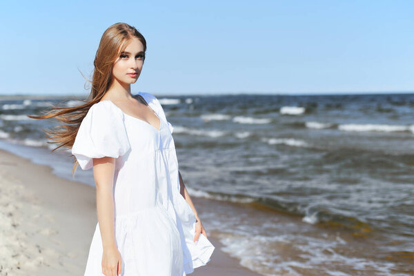 Happy, beautiful woman on the ocean beach standing in a white summer dress. Portrait.