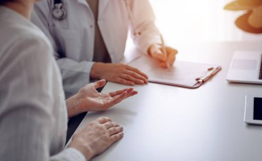 Doktor ve hasta klinikteki masada otururken sağlık muayenesini tartışıyorlar. Kadın hastaların ellerine odaklan, kapat. Mükemmel tıbbi hizmet ve tıp konsepti.