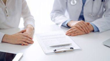 Doktor ve hasta birbirlerine yakın otururken sağlık sorularını tartışıyorlar ve klinikteki masada pano kullanıyorlar, sadece ellerini kapatıyorlar. Tıp konsepti.
