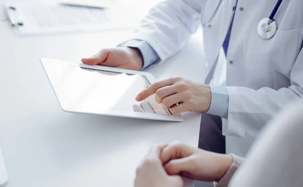 stock image Doctor and patient sitting at the table in clinic. The focus is on female physicians hands using tablet computer, close up. Medicine and healthcare concept.