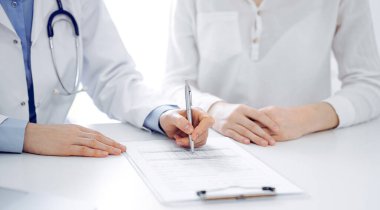 Doktor ve hasta klinikteki masada yan yana oturuyorlar. Kadın doktorların ellerinin tıbbi geçmiş kayıtlarını doldurması ya da kontrol listesi üzerinde yoğunlaşacağız. Kapat. Tıp konsepti.