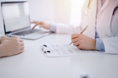 Doktor ve hasta bir şey tartışıyor ve klinikteki masada karşılıklı otururken dizüstü bilgisayar kullanıyorlar. Mükemmel tıbbi hizmet ve tıp konsepti.