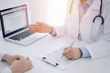 Doktor ve hasta klinikteki masada karşılıklı oturuyorlar. Kadın doktorların ellerinin tıbbi geçmiş kayıtlarını doldurması ya da kontrol listesi üzerinde yoğunlaşacağız. Kapat. Tıp konsepti.