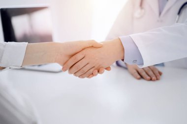 Klinikteki masada karşılıklı otururken doktor ve hasta el sıkışıyor. Sadece eller kapalı. Tıp konsepti.