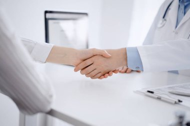 Klinikteki masada karşılıklı otururken doktor ve hasta el sıkışıyor. Sadece eller kapalı. Tıp konsepti.