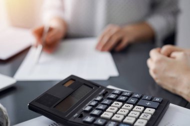 Müşteri ile vergi sayarken ve tartışırken kalem ve dizüstü bilgisayar kullanan kadın muhasebeci, hesap makinesine odaklan. İş denetimi ve finans kavramları.