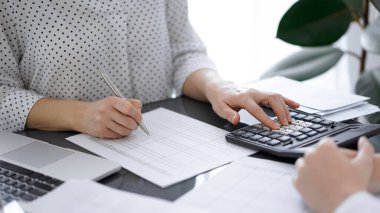 Müşteri ya da meslektaşıyla birlikte vergi sayarken hesap makinesi ve dizüstü bilgisayar kullanan kadın muhasebeci. İş denetleme ekibi, finans danışmanı.