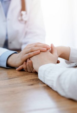 Doktor ve hasta klinikteki ahşap masada oturuyorlar. Kadın doktorların elleri güven veren kadınlarındır. Tıp konsepti.