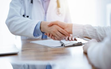 Doktor ve hasta klinikteki ahşap masanın üstünde el sıkışıyor. Tıp konsepti.
