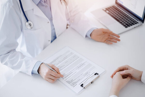 Doctor and patient discussing current health questions while sitting opposite of each other and using clipboard at the table in clinic, just hands closeup. Medicine concept.