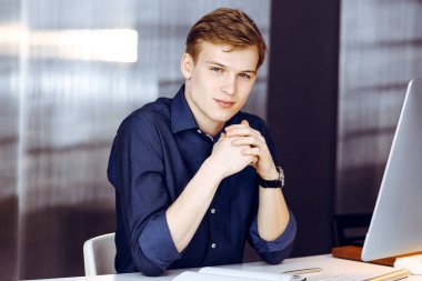 Genç sarışın işadamı iş yerinde bilgisayarla strateji düşünüyor. Girişim işi, başarı için çok çalışmak ve zamanın dışında çalışmak demektir..