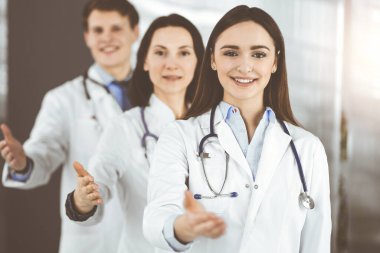 Doktorlar el sıkışmak ya da insanların hayatını kurtarmak için yardım eli uzatırken takım olarak duruyorlar. Tıbbi yardım, sağlık sigortası, en iyi hastalık tedavisi ve ilaç konsepti.