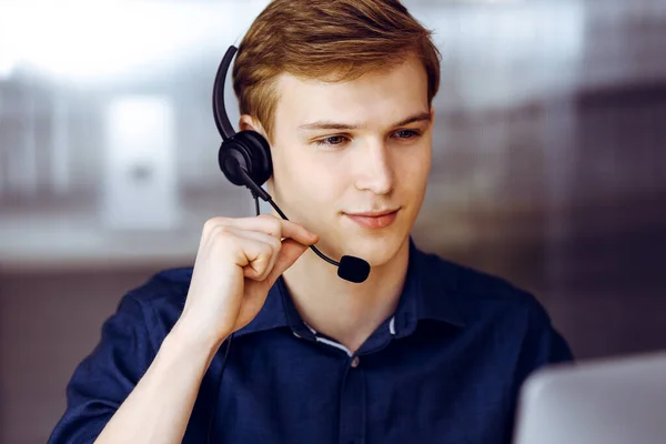Young blond businessman using headset and computer at work. Startup business means working hard and out of time for success achievement.