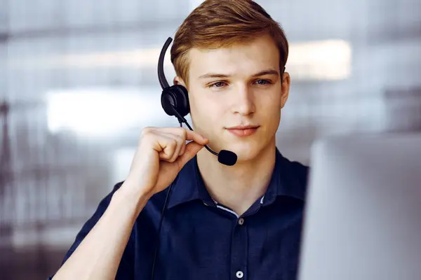 Young blond businessman using headset and computer at work. Startup business means working hard and out of time for success achievement.