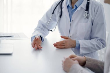 Doktor ve hasta klinikteki masada otururken güncel sağlık sorularını tartışıyorlar, sadece eller kapalı. Tıp konsepti.
