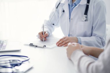 Doktor ve hasta klinikteki masada oturuyor. Kadın doktorların ellerinin tıbbi geçmiş kayıtlarını doldurması ya da kontrol listesi üzerinde yoğunlaşacağız. Kapat. Tıp konsepti.