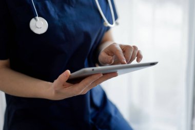 Doktor kadın panorama penceresinin yanında dururken tablet bilgisayar kullanıyor, kapatın. Doktor ya da cerrah iş başında. Tıp konsepti.