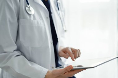 Doktor kadın panorama penceresinin yanında dururken tablet bilgisayar kullanıyor, kapatın. Doktor ya da cerrah iş başında. Tıp konsepti.