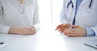 Doktor ve hasta klinikteki masada yan yana otururken sağlık sorunlarını tartışıyorlar. Sadece ellerinizi yakın tutun. Tıp konsepti.