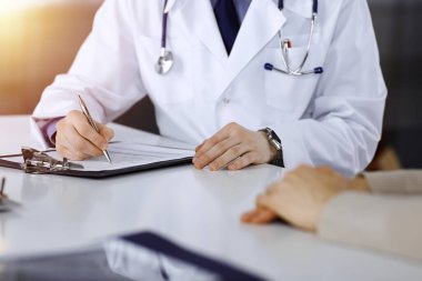 Bilinmeyen bir erkek doktor ve hasta kadın karanlık bir klinikte otururken bir şey tartışıyorlar ve arka planda pano kullanıyorlar..