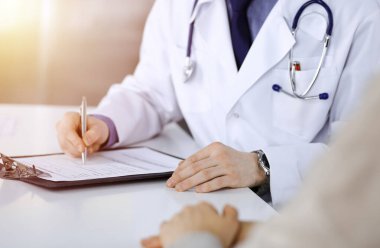 Bilinmeyen bir erkek doktor ve hasta kadın karanlık bir klinikte otururken bir şey tartışıyorlar ve arka planda pano kullanıyorlar..