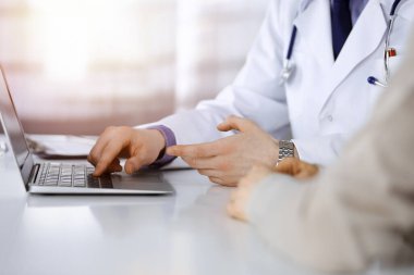 Bilinmeyen bir erkek doktor ve hasta kadın karanlık bir klinikte dizüstü bilgisayar kullanırken bir şey tartışıyorlar..