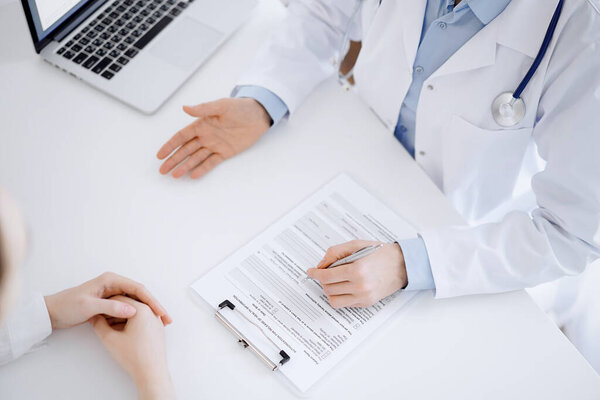 Doctor and patient discussing current health questions while sitting opposite of each other and using clipboard at the table in clinic, just hands closeup. Medicine concept.