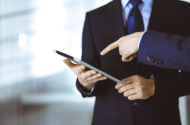 İş adamları yeni projelerini tartışmak için bir tablet bilgisayar kullanıyorlar, modern bir ofiste duruyorlar. İş yerinde iş arkadaşı olan tanınmamış bir işadamı ya da erkek girişimci