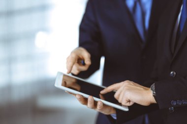 İş adamları yeni projelerini tartışmak için bir tablet bilgisayar kullanıyorlar, modern bir ofiste duruyorlar. İş yerinde iş arkadaşı olan tanınmamış bir işadamı ya da erkek girişimci