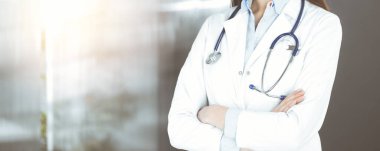 Kimliği belirsiz genç bir kadın doktor güneşli klinikte kollarını kavuşturmuş duruyor. Coronavirus salgını sırasında ilaç konsepti. Covid 2019.