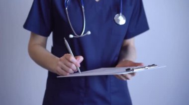 Doktor kadın tıbbi not almak için pano kullanıyor. Gri arkaplanın yanında duruyor. Kapat. Doktor ya da cerrah iş başında. Tıp konsepti.