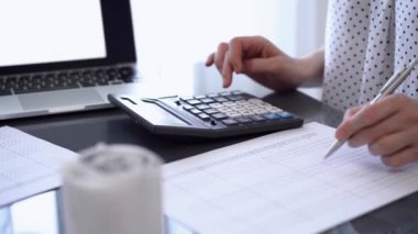 İki muhasebeci, faturalar hesaplanmayı beklerken vergi veya gelir dengesi hesaplamak için bir hesap makinesi ve dizüstü bilgisayar kullanıyor. İş denetimi ve vergi kavramları.