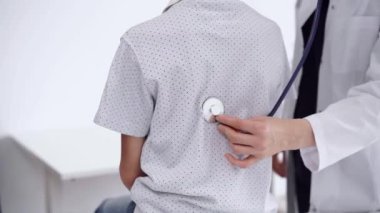 Doktor ve çocuk hasta klinikte. Beyaz önlüklü bir doktor steteskopla genç bir çocuğu muayene ediyor. İlaç, terapi konsepti.